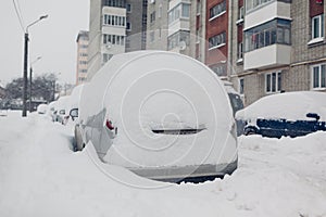 Badly cleaned roads after snow storm. Cars covered with snow in city. Automobiles stuck in heaps after winter blizzard