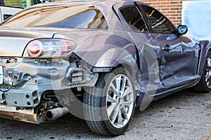 Badly wrecked silver car that can still be driven parked at store - Right rear view - where it has been hit