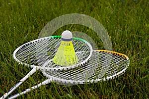 Badminton set yellow shuttlecock and rackets lying on green grass. Sports concept.