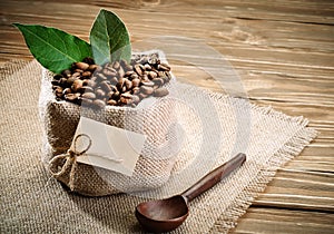 Bag of burlap filled with coffee beans on wooden background.