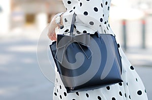 Bag close-up in female hands. Black and white image style. Girl in summer dress with polka dots and a black bag with a bow. Woman