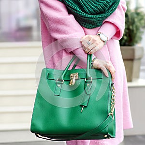 Bag close-up in female hands. Stylish modern and feminine image, style. Girl with a green bag in a pink coat