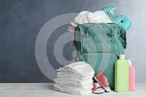 Bag with diapers and baby accessories on white wooden table against grey background. Space for text photo