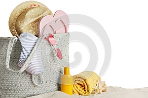 Bag with different beach objects on sand against white background