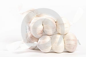 Bag filled with white garlic bulbs resting on a plain white background