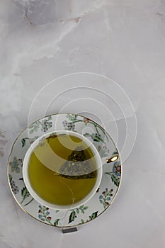 Bag of green tea with water in a porcelain cup