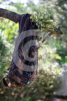 The bag hangs on the tree. Traveler`s backpack with bouquet of wild flowers