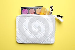 Bag with hygienic lipsticks and cosmetic products on yellow background