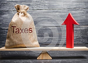 A bag with the inscription taxes and a red arrow up on the scales. The concept of profit growth and the economy by reducing