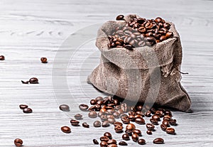 Bag made from burlap cloth with coffee beans and some grains lying near it on the light background