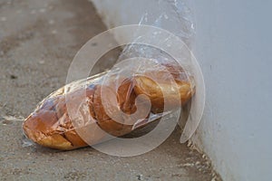 A bag made of transparent plastic containing white buns. It rests against a white wall. Perhaps left to people or