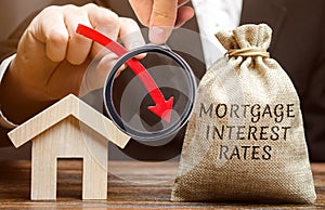 Bag with the money and the word Mortgage interest rates and arrow down and house. Low interest in mortgages. Reducing interest