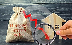 Bag with the money and the word Mortgage interest rates and arrow to down and house. Low interest in mortgages. Reducing interest