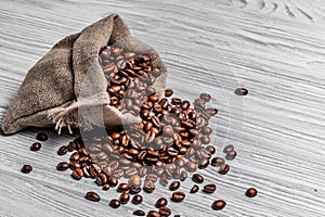 Bag of natural brown coffee beans and some scattered seeds on the light wooden background