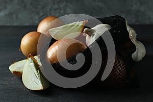 Bag with onion and garlic on black wooden table