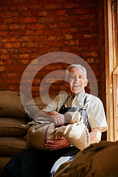 We bag our own beans. Cropped portrait of a senior man holding a sack of coffee beans while sitting in a roastery.