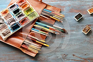 Bag with paint brushes and watercolors on wooden table