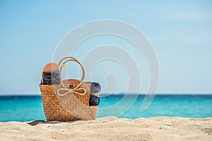 A bag on a tropical beach. Sunglasses and flip-flops in a woven bag on white sand against the background of the sea or