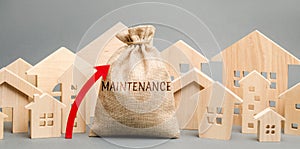 A bag with the word Maintenance, wooden houses and up arrow. Rising costs for the maintenance of housing, large bills. Expensive