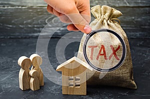 A bag with the word Tax and family stand near the house. Taxes on real estate, payment. Penalty, arrears. Register of taxpayers