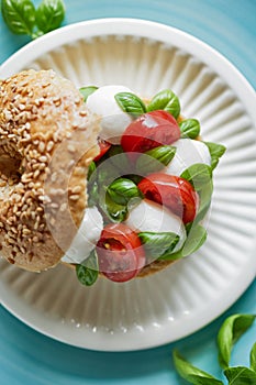 Bagel with caprese salad; cherry tomatoes, mini mozzarella cheese and basil leaves drizzled with olive oil served on a white plate
