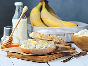 Bagel with cottage cheese , banana and honey. Concept of healthy breakfast. White wooden background.