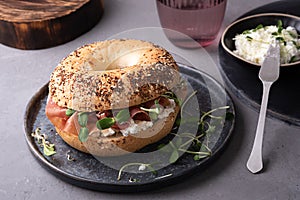 Bagel with cream cheese, dry cured ham and microgreens on a plate on a gray background, breakfast sandwich