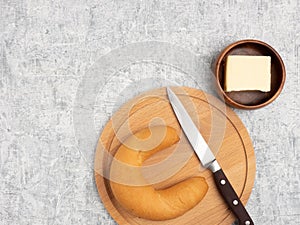 Bagel on cutting board, butter, knife on white concrete background