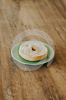 A bagel on a green plate on a wooden table, with golden brown, and cut in half