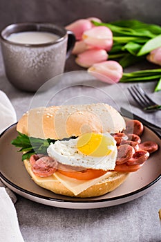 Bagel with heart-shaped boiled egg, tomato, cheese and herbs on a plate. Vertical view