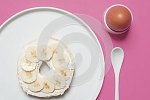 Bagel on a plate with a boiled egg on a pink background