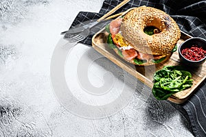 Bagel sandwich with salmon, cream cheese, spinach and egg on a wooden plate. Gray background. Top view. Copy space