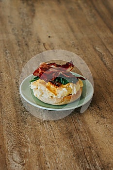 A bagel sandwich with scrambled eggs, bacon, and spinach on a green plate