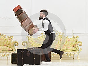 Baggage insurance concept. Porter, butler accidentally stumbled, dropping pile of vintage suitcases. Man with beard and