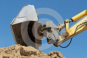 Excavator bucket over earth heap against a blue sky