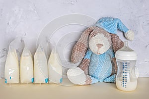 Bags with breast milk with knitted toy. Breast pump on yellow background. Milk bank. Expressing breast milk. Breast-feeding.