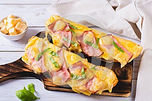 Baguette baked with ham, cheese and basil on a wooden board