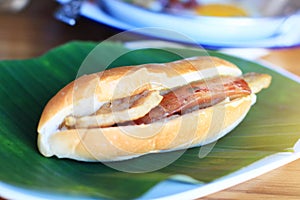 Baguette bread sandwich with cheese, ham on fresh Green banana leaf on wooden table in homemade