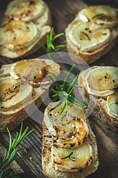 Baguette bread slices baked with goat cheese and honey, decorated with rosemary, on wooden background