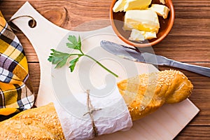 Baguette, butter, knife and parsley on a cutting board