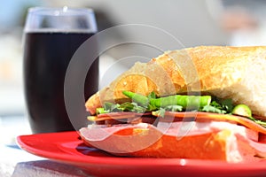 Baguette sandwich cut in half with ham, turkey breast, cheese, lettuce and tomatoes on a cutting board closeup