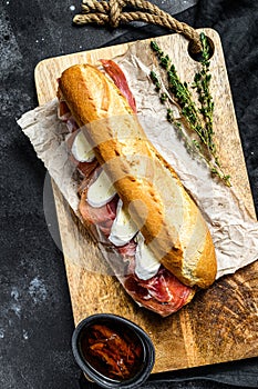 Baguette sandwich with jamon ham serrano, paleta iberica, Camembert cheese on the cutting Board. Black background, top view photo