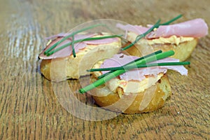 Baguette slices with cheese spread, ham and chives.