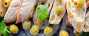 Baguette stuffed with olives, cut with fresh green olives and parsley, served on a stone plate