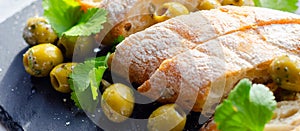 Baguette stuffed with olives, cut with fresh green olives and parsley, served on a stone plate