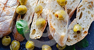 Baguette stuffed with olives, cut with fresh green olives and parsley, served on a stone plate