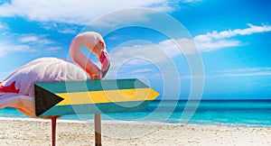 Bahamas flag on wooden table sign on beach background with pink flamingo. There is beach and clear water of sea and blue sky in