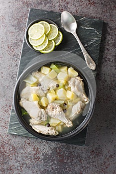 Bahamian Chicken Souse with chicken wings, potatoes, celery, lime and spices closeup on the plate. Vertical top view