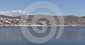 Baikal lake spring landscape view. Snow-covered shore of the lake. Rocky forested coastline.