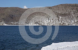 Baikal lake spring landscape view. Snow-covered shore of the lake. Rocky forested coastline.